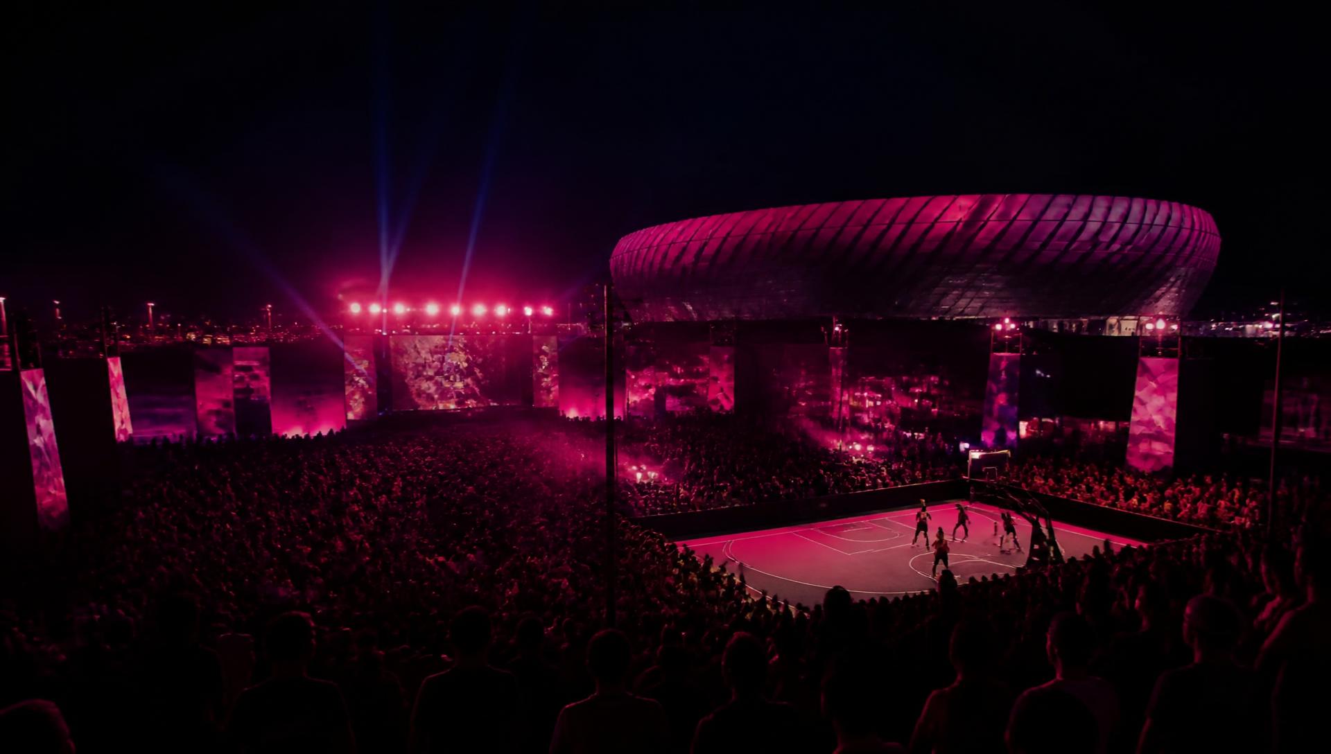 Aficionados en una fan zone junto a un estadio de fútbol iluminada en fucsia (imagen provisional)